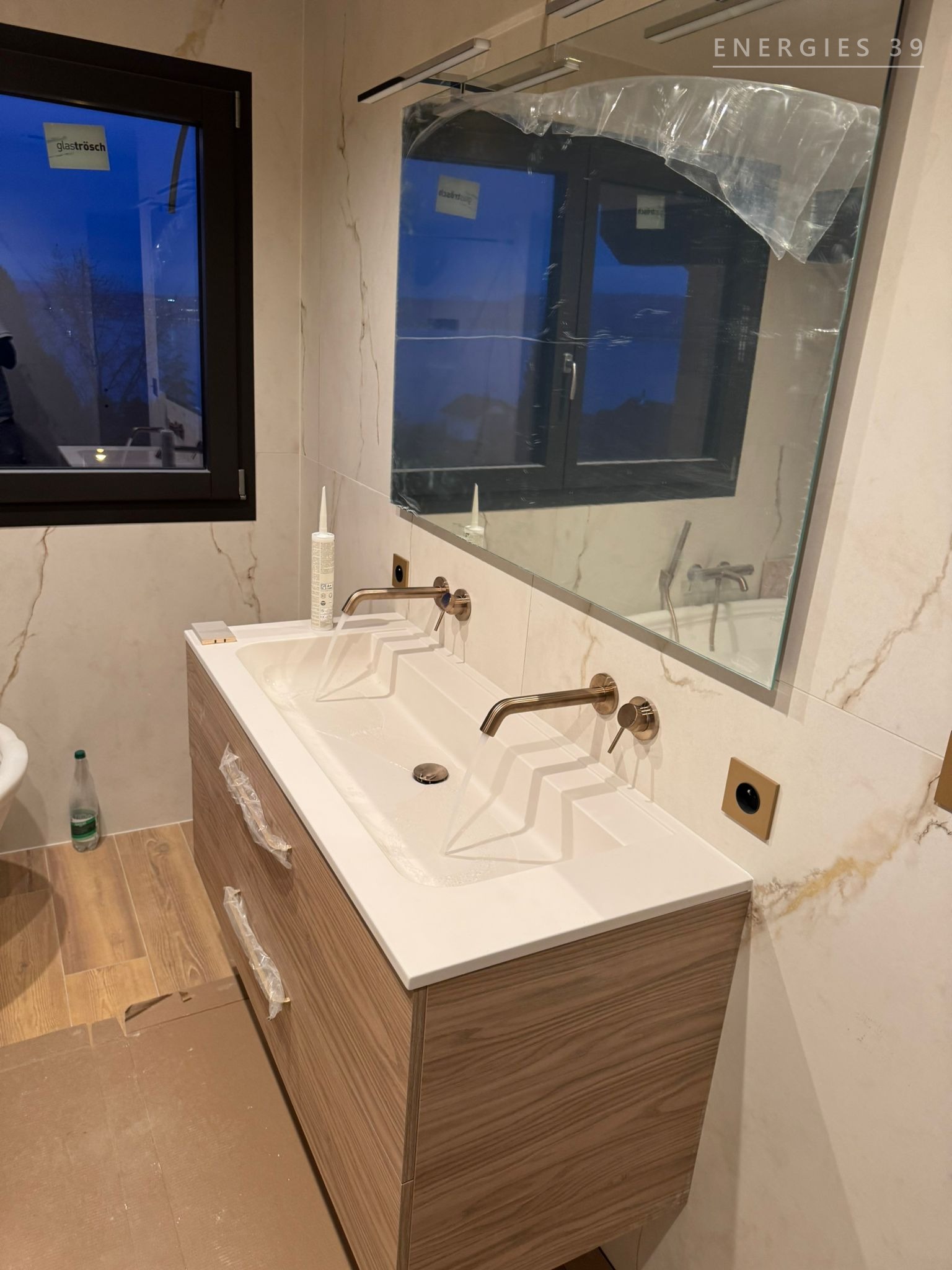 Détail d'une double vasque en bois avec robinetterie murale bronze brossé