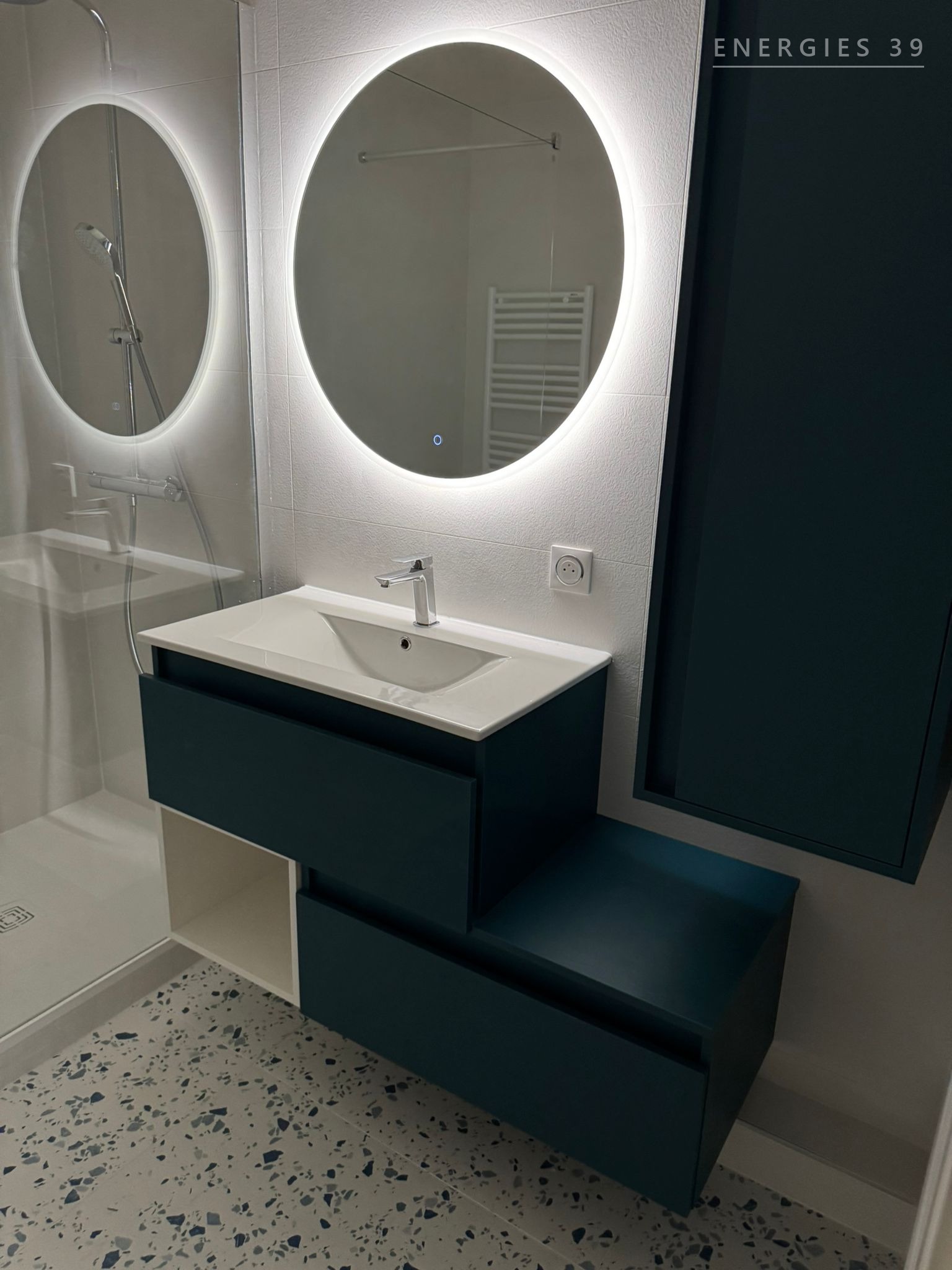 Vasque suspendue bleu canard avec miroir rond rétro-éclairé sur sol terrazzo