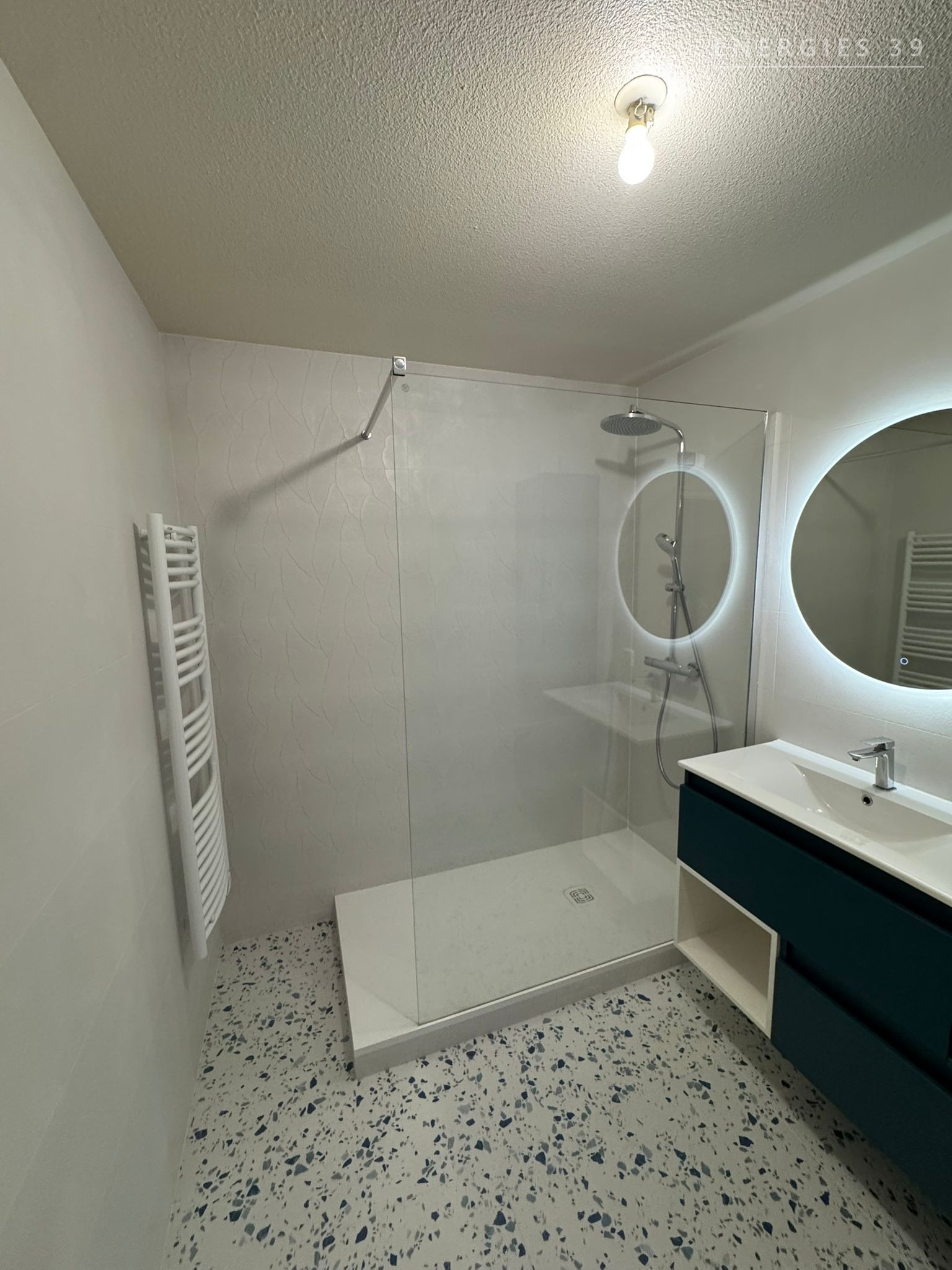 Salle de bain design avec sol terrazzo, vasque bleu canard et miroir rond rétro-éclairé